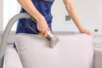 Janitor cleaning the upholstery of a fabric chair with a machine.
